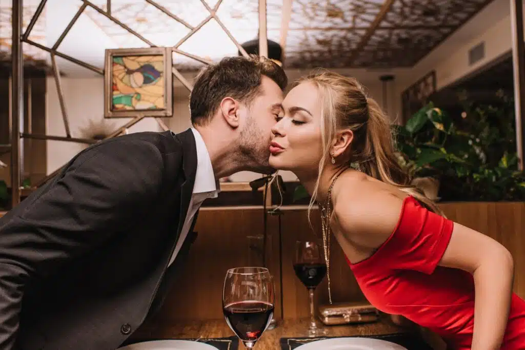 attractive girl kissing cheek of man in restaurant on valentines day